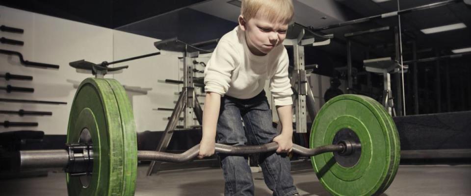 Determined young boy trying to lift a heavy weight bar