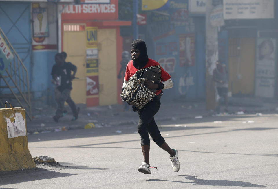 A looter runs with bag during anti-government protests in Port-au-Prince, Haiti, Friday, Oct. 11, 2019. Protesters burned tires and spilled oil on streets in parts of Haiti's capital as they renewed their call for the resignation of President Jovenel Moïse just hours after a journalist was shot to death. (AP Photo/Rebecca Blackwell)