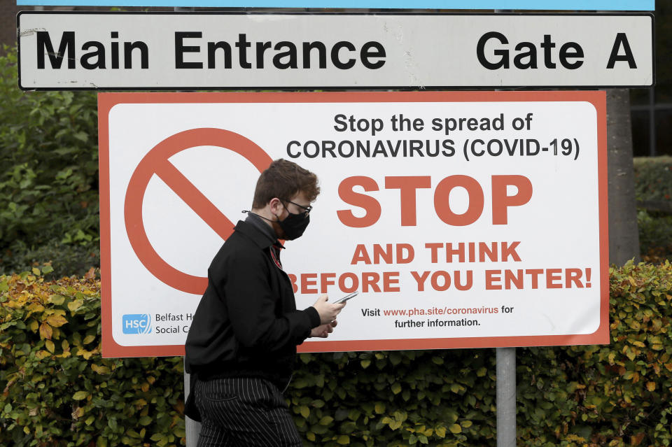 A man wearing a face mask walks past an entrance to Belfast City Hospital, Northern Ireland, Wednesday, Oct. 14, 2020. Northern Ireland introducing the tightest COVID-19 restrictions in the United Kingdom on Wednesday, closing schools for two weeks and pubs and restaurants for a month. “This is not the time for trite political points," First Minister Arlene Foster told lawmakers at the regional assembly in Belfast. “This is the time for solutions." (Brian Lawless/PA via AP)