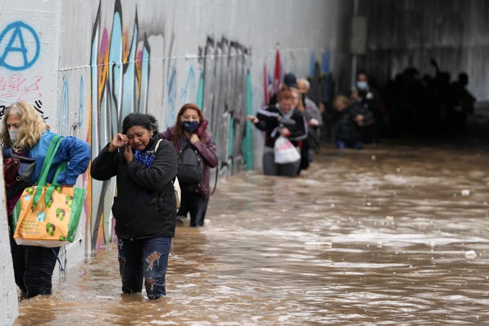 Passengers wade through high water after evacuating a bus stuck in a flooded underpass in southern Athens, Thursday, Oct. 14, 2021. Storms have been battering the Greek capital and other parts of southern Greece, causing traffic disruption and some road closures. (AP Photo/Thanassis Stavrakis)