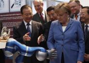 Chinese Premier Wen Jiabao (L) watches as German Chancellor Angela Merkel touches a robotic hand at the stand of Harbin Institute of Technology during their opening tour at the Hanover industrial fair in Hanover, April 23, 2012.