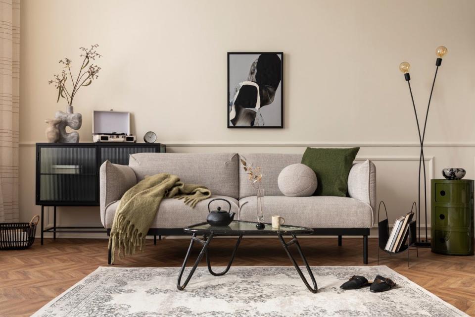 Gray couch in front of black metal and glass table in front of a beige wall with artwork
