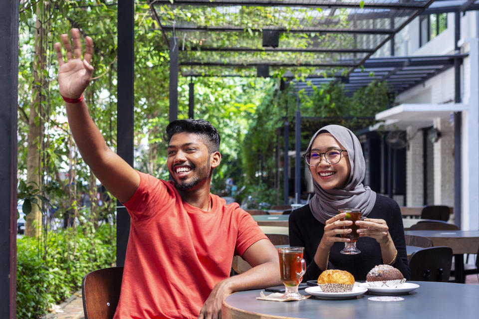 happy multi ethnic couple waving hand and smiling while having afternoon tea