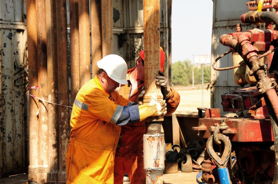 Workers wearing personal protective equipment get caught in mud while working on a drilling platform.