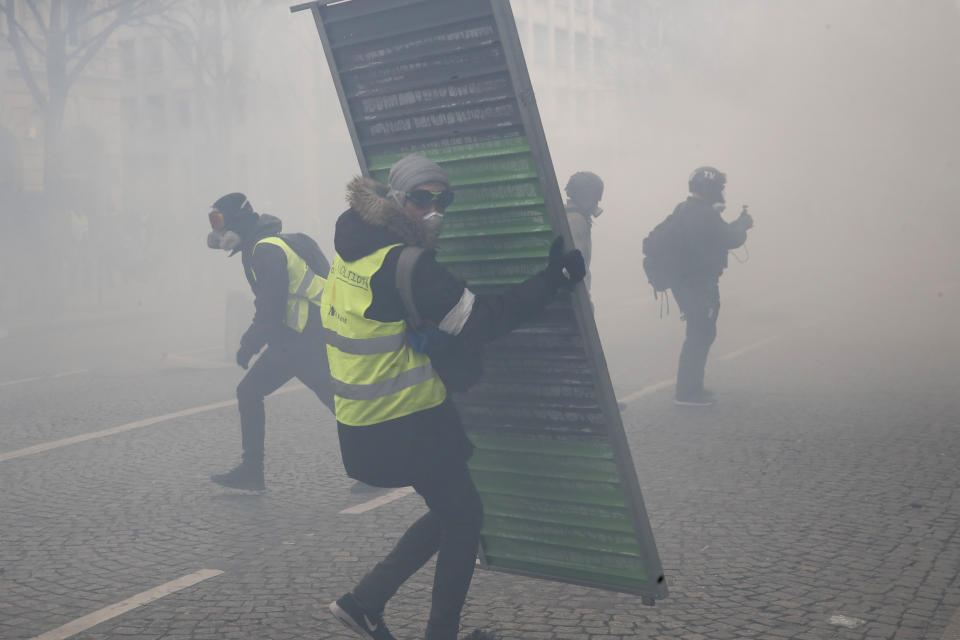 Protesters set up barricades through tear gas during a yellow vests demonstration Saturday, March 16, 2019 in Paris. French yellow vest protesters clashed Saturday with riot police near the Arc de Triomphe as they kicked off their 18th straight weekend of demonstrations against President Emmanuel Macron. (AP Photo/Christophe Ena)