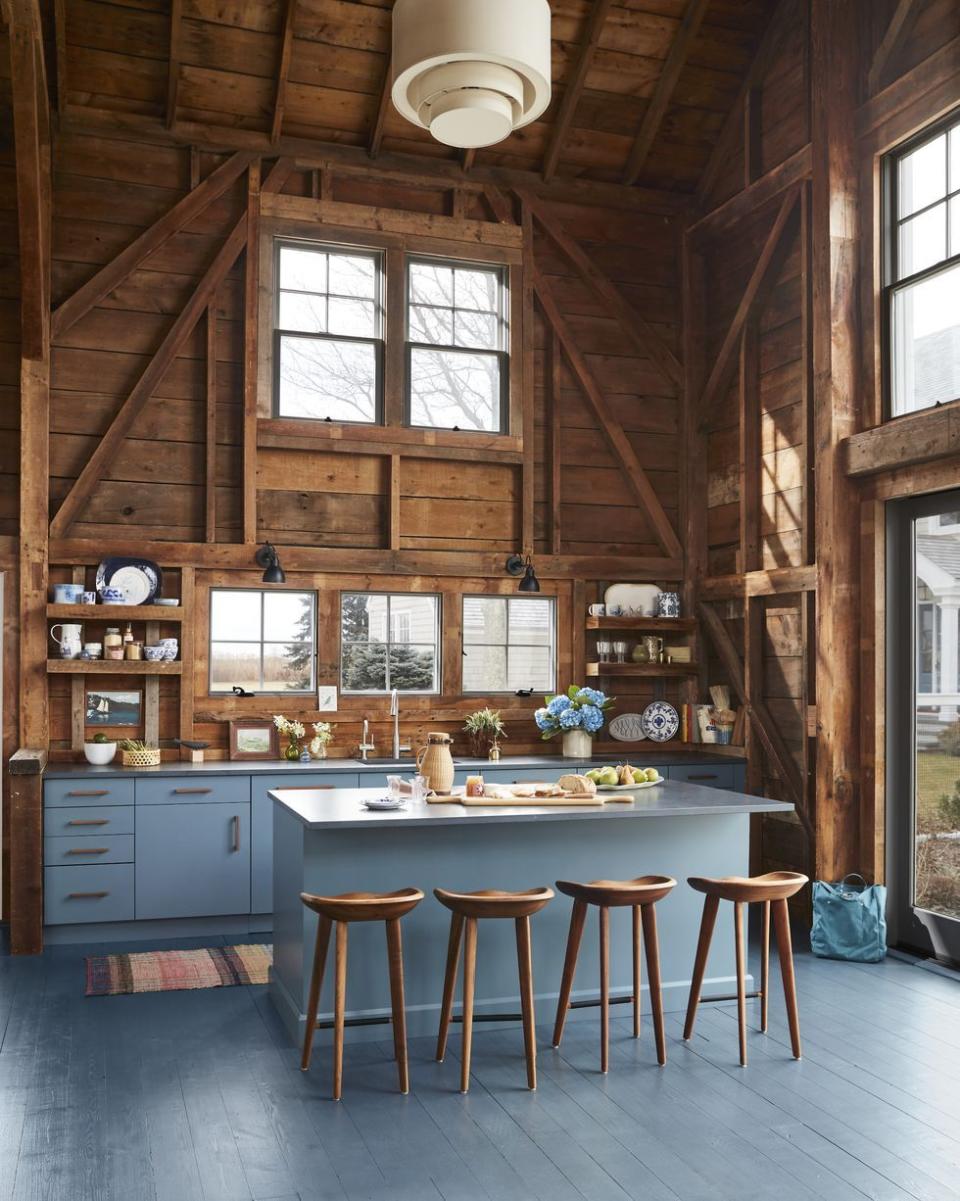 rustic kitchen with blue painted floor and blue cabinets paired with natural wood walls, ceiling, and barstools
