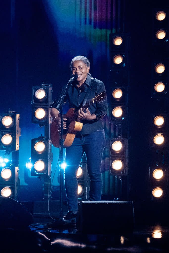 tracy chapman playing guitar and singing in front of yeloow stage lights at the grammy awards