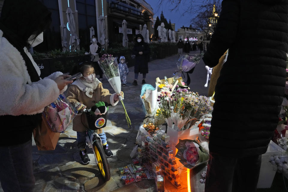 A child wearing mask buys flowers from a pop-up store at a mall with shops re-opening for business as restrictions are eased in Beijing, Saturday, Dec. 3, 2022. Chinese authorities on Saturday announced a further easing of COVID-19 curbs with major cities such as Shenzhen and Beijing no longer requiring negative tests to take public transport. (AP Photo/Ng Han Guan)