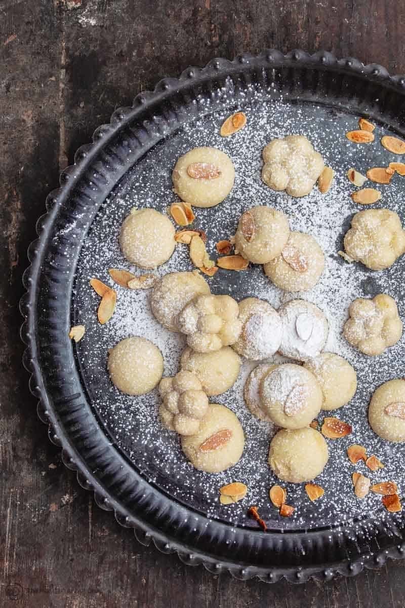 A selection of dusted pastries with nuts on a dark round tray