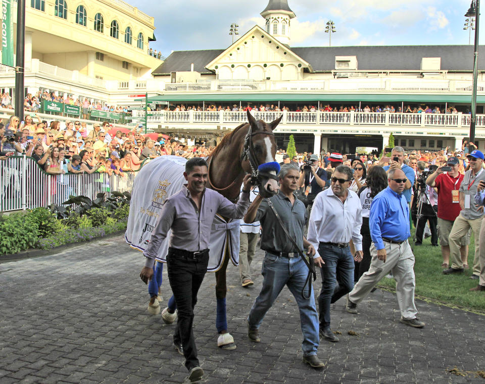 FILE - In this June 16, 2018, file photo, Triple Crown champion Justify, led by exercise rider Humberto Gomez, left, and groom Eduardo Luna, second from left, is the center of attention in the paddock at Churchill Downs in Louisville, Ky. The undefeated Triple Crown winner has been retired from racing because of fluid in his left front ankle, trainer Bob Baffert and Justify’s owners announced Wednesday, July 25, 2018. They cited caution over the horse’s ankle making it impossible to tell if he’d be able to race by the fall. (AP Photo/Garry Jones, File)