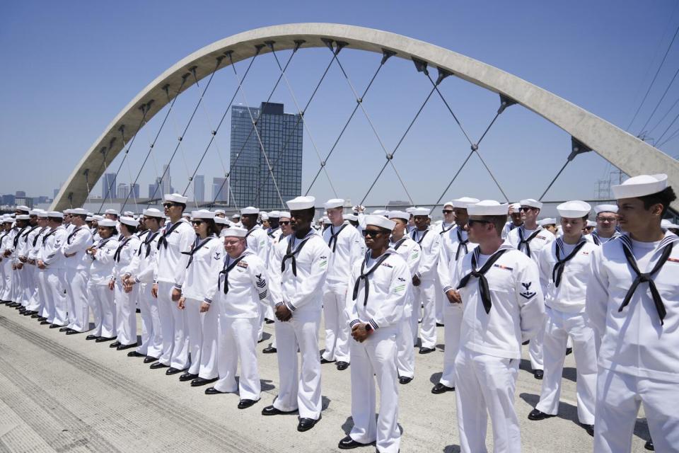 People in white uniforms stand in several rows on a road.