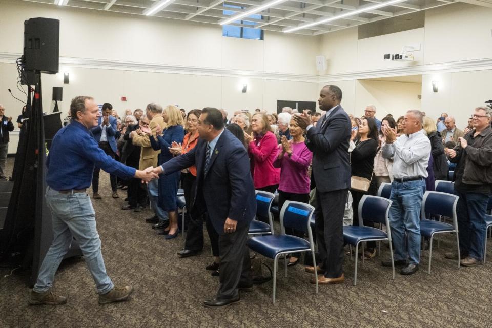 Adam Schiff shakes hands with a man in the front row as a standing crowd applauds