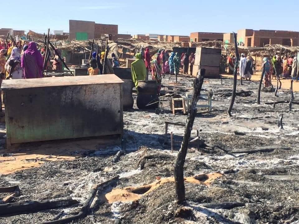 In this Sunday, Dec. 29, 2019 photo, residents of a refugee camp gather around the burned remains of makeshift structures, in Genena, Sudan. A Sudanese aid group says sporadic tribal clashes between Arabs and non-Arabs are continuing in Sudan’s West Darfur province. Adam Regal, a spokesman for the aid group, said Tuesday that the death toll has climbed to least two dozen people, including children. He says some of those killed were burned to death. (Organization for the General Coordination of Camps for Displaced and Refugees via AP)