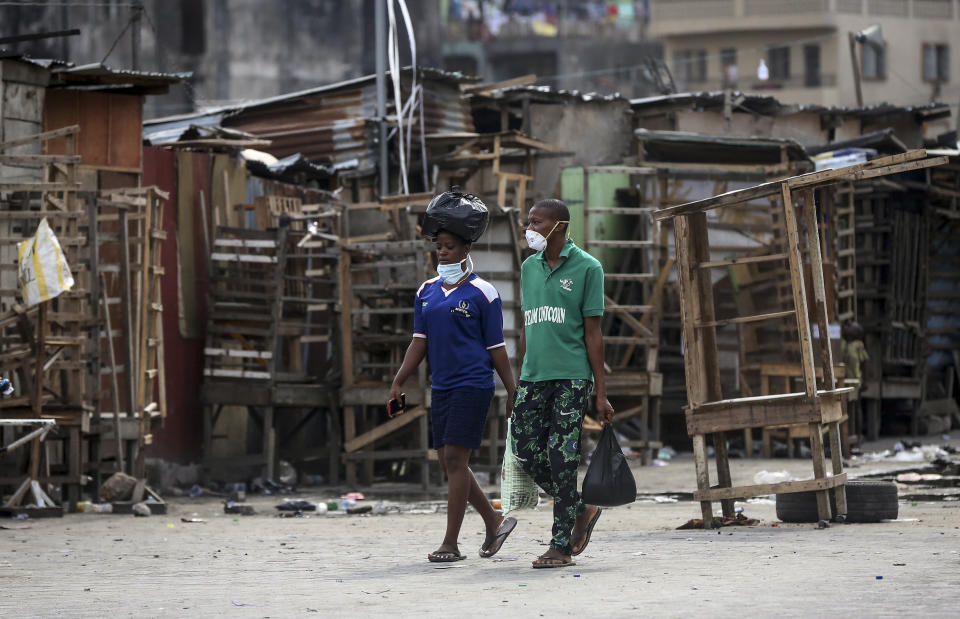 People wearing face masks walk past closed street stalls and shops due to a government ban on the operation of non-essential businesses and markets to halt the spread of the new coronavirus, in Lagos, Nigeria Thursday, March 26, 2020. (AP Photo/Sunday Alamba)