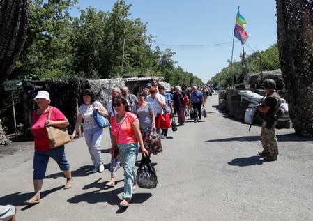 People cross the contact line between pro-Moscow rebels and Ukrainian troops as a member of the Ukrainian State Border Guard Service stands guard