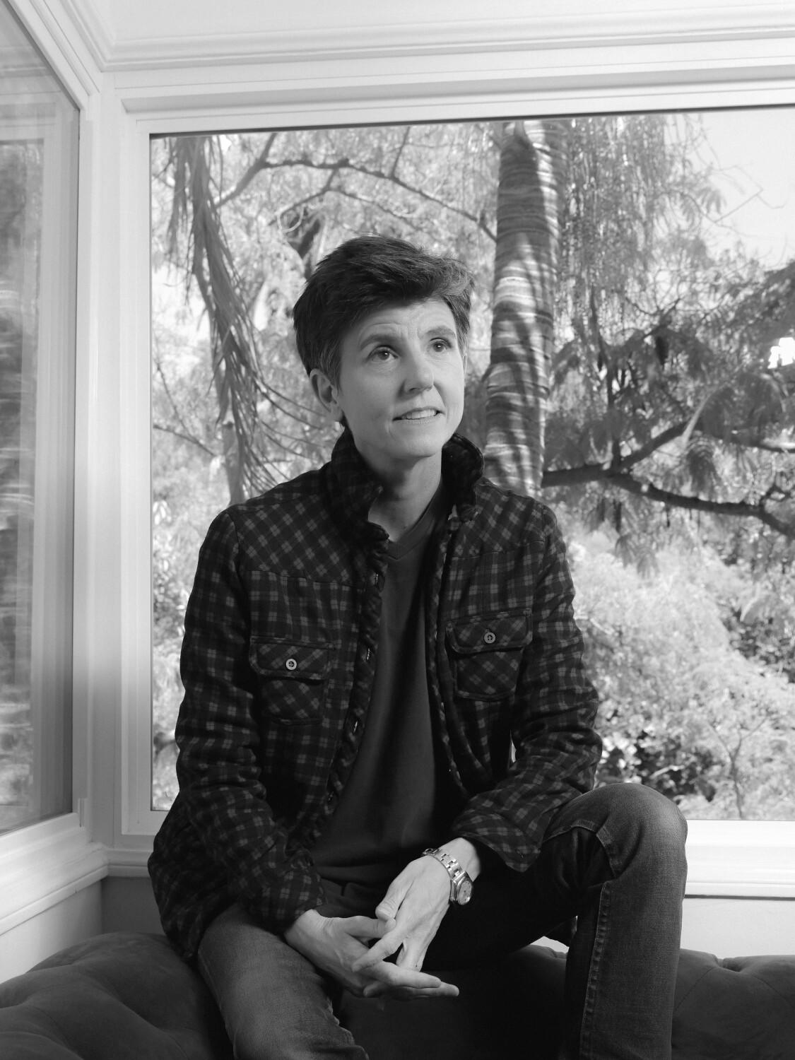 A woman wearing a flannel sits by a window.