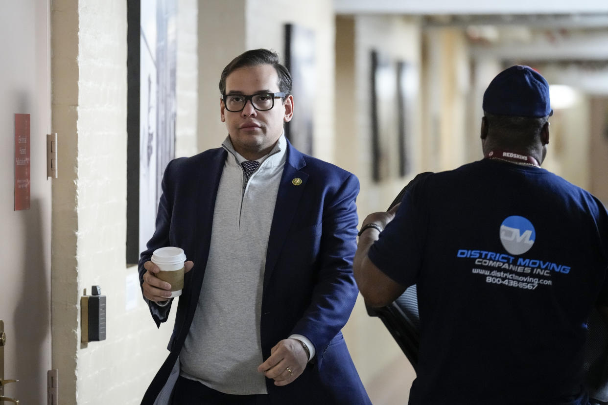 Rep. George Santos, holding a cup of coffee, walks down a corridor, passing a man wearing a blue uniform marked District Moving. (Photo by Drew Angerer/Getty Images)