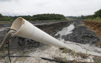 FILE - In this Friday June 26, 2015 file photo, a drain pipe sticks out of a coal ash retention pond at the Dominion Power's Possum Point Power Station in Dumfries, Va. The company is moving coal ash from several ponds to one lined pond. As Virginia and its public utilities struggle to cope with the coal ash buried in pits and ponds across the state, tons more of the industrial byproduct is being imported each year. (AP Photo/Steve Helber, File)