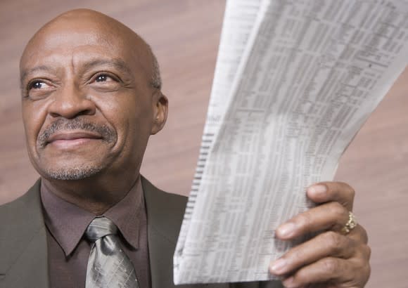 A smiling older man holding a newspaper with stock listings