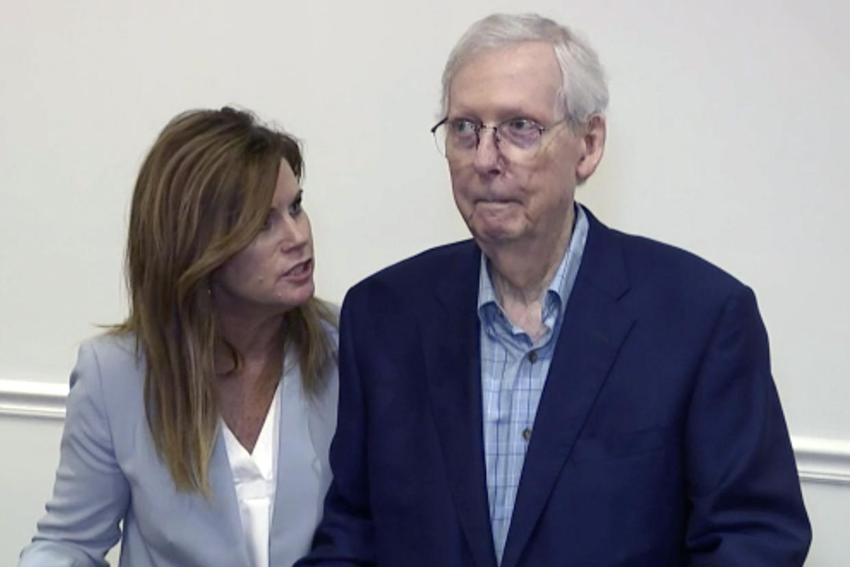 An aide looks at Senate Minority Leader Mitch McConnell as he stares straight ahead.