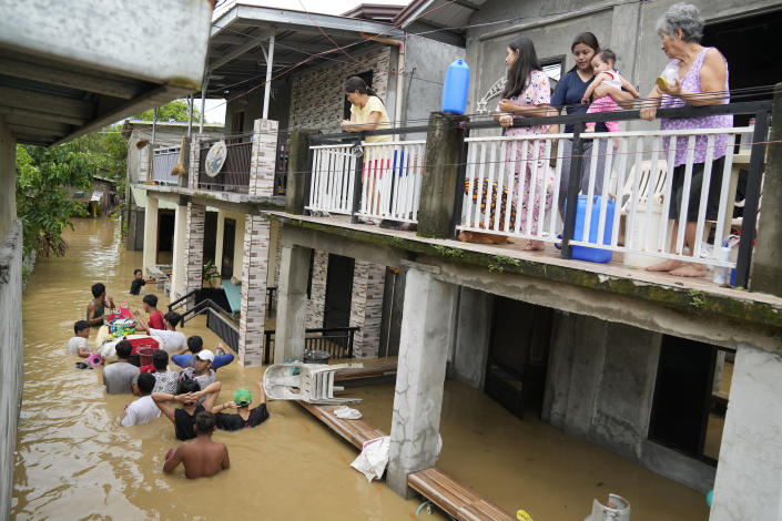 Residents stay on the deck of their house as others negotiate a flooded road due to Typhoon Noru in San Miguel town, Bulacan province, Philippines, Monday, Sept. 26, 2022. Typhoon Noru blew out of the northern Philippines on Monday, leaving some people dead, causing floods and power outages and forcing officials to suspend classes and government work in the capital and outlying provinces. (AP Photo/Aaron Favila)