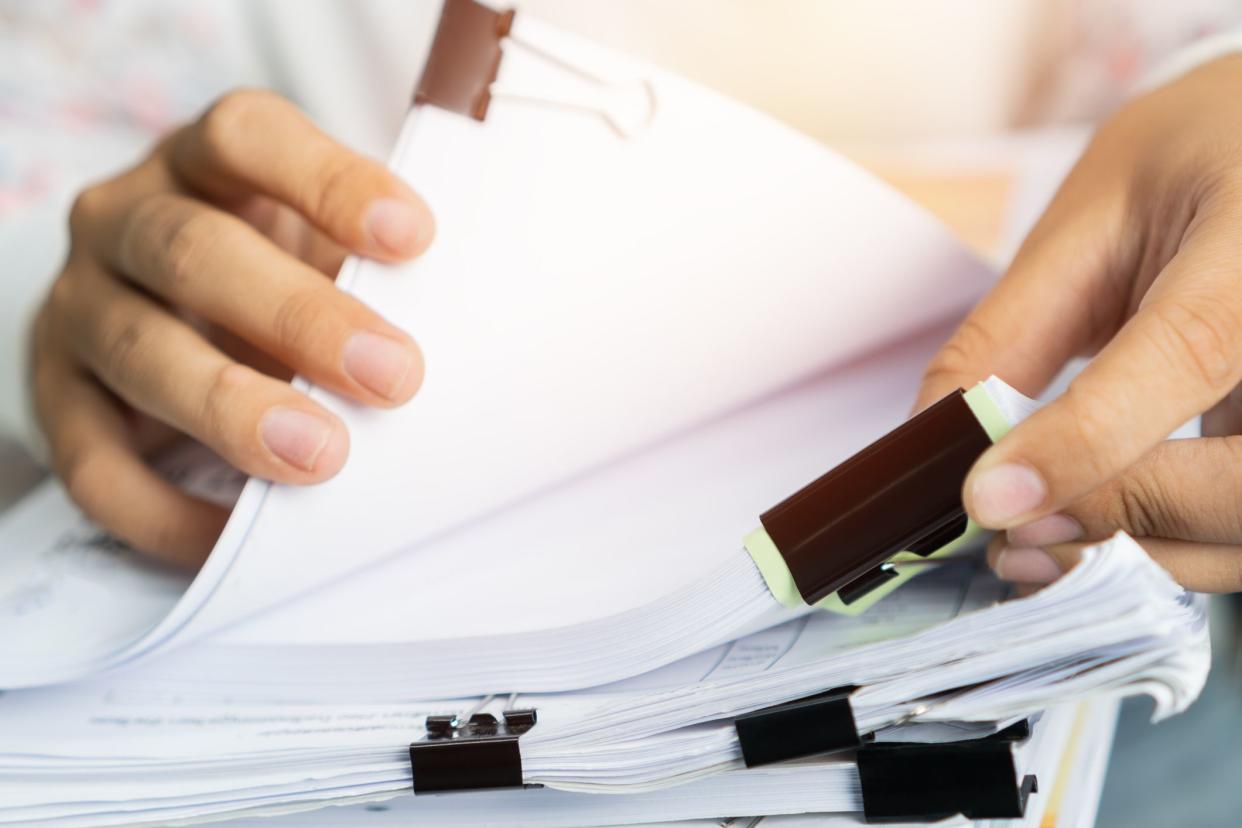 Closeup of two hands going through a stack of paperwork, in bundles with black binder clips, blurred background of midsection a person