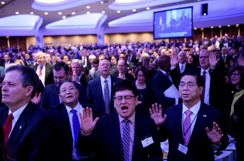 A crowd of hundreds of mostly older people stand singing and praying