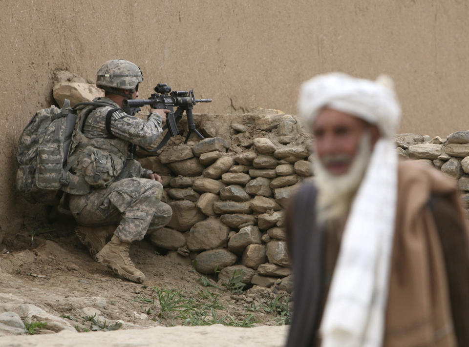 FILE - In this May 1, 2009, file photo, an Afghan man looks on as U.S. solider's of 3rd Brigade, 10th Mountain Division stands guard during a search operation in Nerkh district of Wardak province in west of Kabul, Afghanistan. A burst of strength by al-Qaida that is chipping away at the remains of Mideast stability now confronts President Barack Obama, testing his hands-off approach to conflicts in Iraq and Syria at the same time he pushes to keep thousands of U.S. forces in Afghanistan. Obama has already decided the fight against extremists must continue, so long as Afghan President Hamid Karzai signs off on a joint security agreement. (AP Photo/Rafiq Maqbool, File)