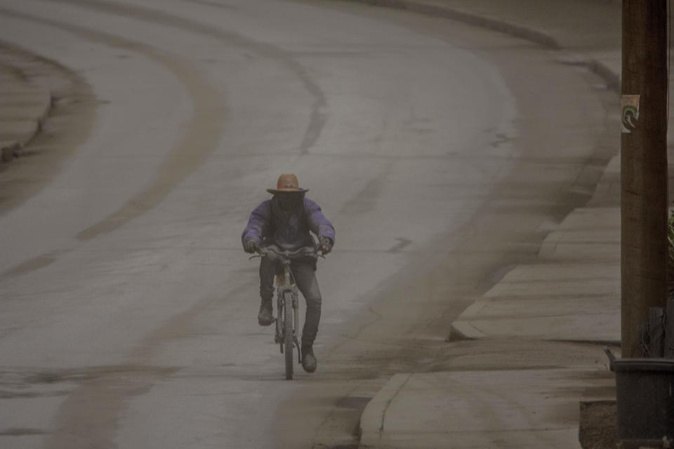 A man rides his bicycle along the main Black Rock road, covered with ash coming from the eruption of La Soufriere volcano in the neighboring island of St. Vincent, on the outskirts of Bridgetown, Barbados, Sunday, April 11, 2021. La Soufriere's volcanic history could inform St. Vincent’s residents as they recover from the recent eruptions. In the meantime, unlike their ancestors, they are getting continual updates and guidance. (AP Photo/Chris Brandis)