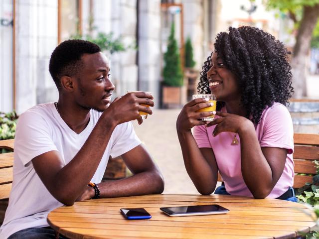 Portrait of stylish black couple talking to each other at summer street cafe