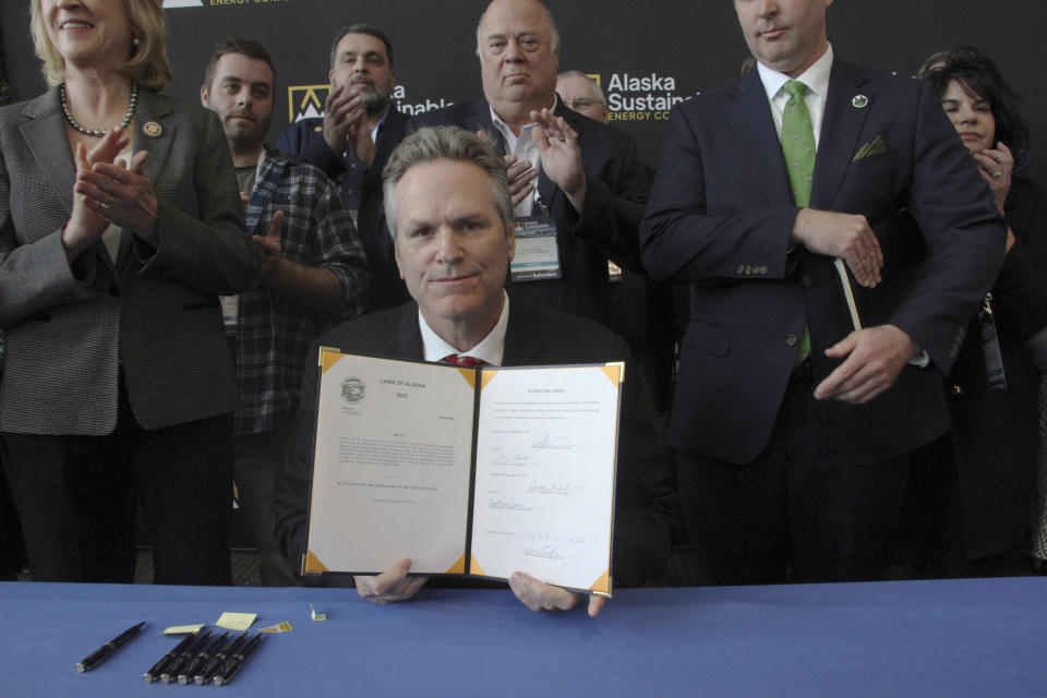 Alaska Gov. Mike Dunleavy displays a bill he had just signed that would allow the state to set up a carbon offset program, Tuesday, May 23, 2023, in Anchorage, Alaska. Dunleavy signed the bill with Alaska lawmakers and administration officials standing behind him during the Alaska Sustainable Energy Conference at the Dena'ina Civic and Convention Center in downtown Anchorage. (AP Photo/Mark Thiessen)