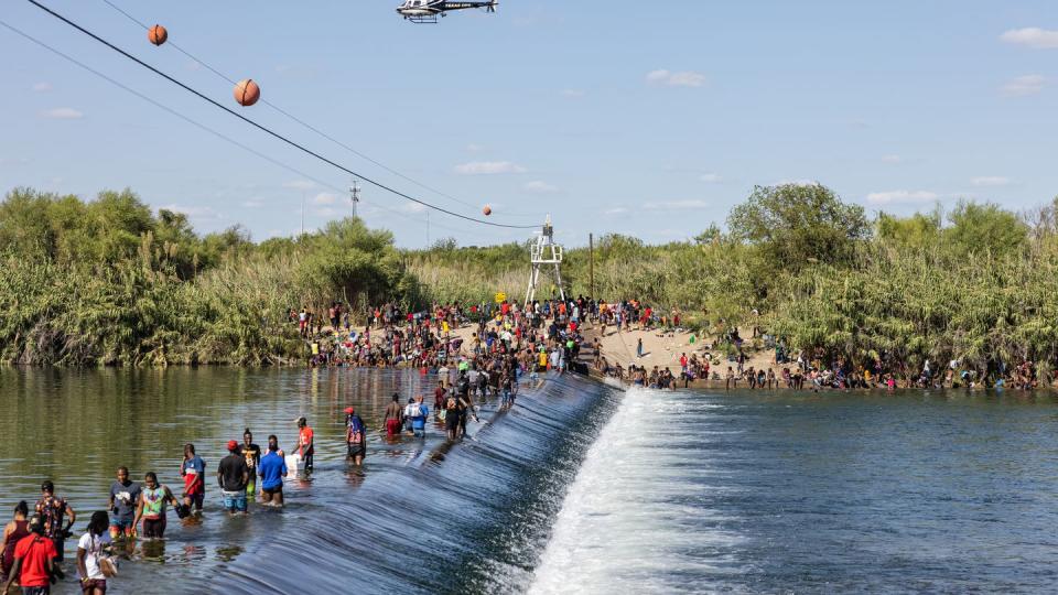 Haitian migrants gather along the banks of the Rio Grande as a Texas Department of Safety helicopter flies overhead in Del Rio on Thursday, Sept.16, 2021. (Jordan Vonderhaar for The Texas Tribune)