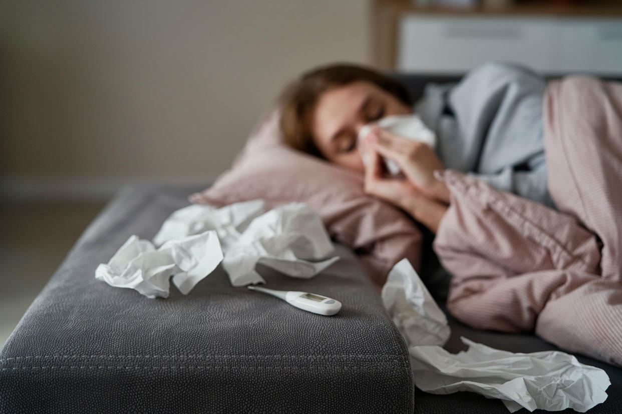 Young woman with high temperature and flu lying down on sofa Getty Images/gpointstudio