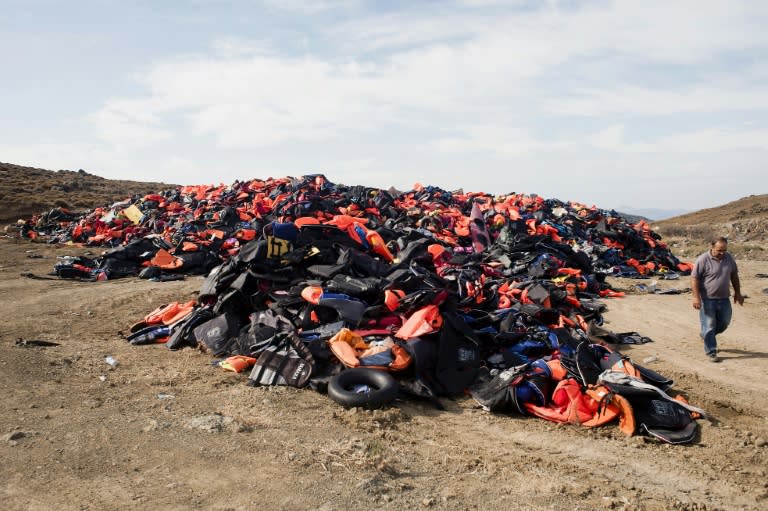 A municipality employee walks past a pile of lifejackets discarded by migrants and refugees in the village of Molyvos, on the Greek island of Lesbos