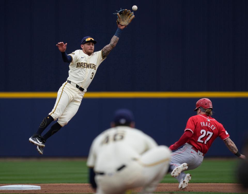 Brewers shortstop Joey Ortiz leaps for a throw from catcher Eric Haase as Cincinnati's Jake Fraley slides safely into second base during the first inning Monday in Phoenix, Ariz.