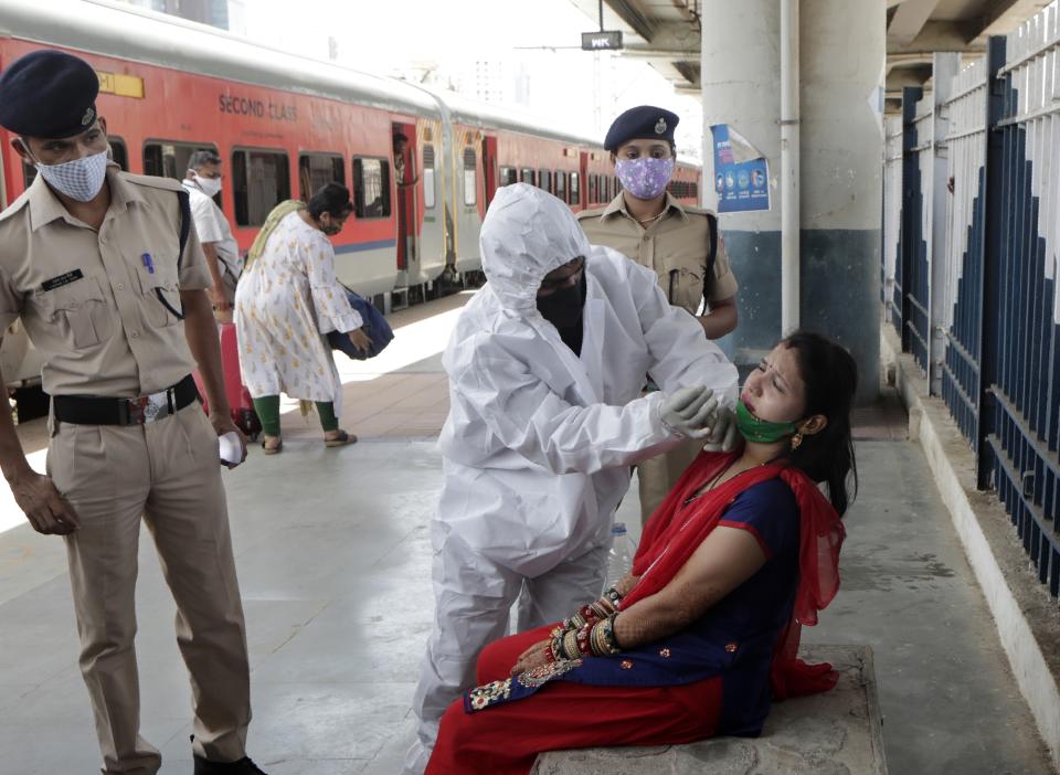 A health worker collects swab sample of traveler to test for COVID-19 at train station in Mumbai, India, Monday, May 24,2020. India crossed another grim milestone Monday of more than 300,000 people lost to the coronavirus as a devastating surge of infections appeared to be easing in big cities but was swamping the poorer countryside. (AP Photo/Rajanish kakade)