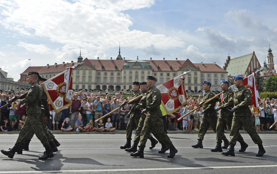 Polish Army soldiers holding military unit banners march on one of the city's main streets during a yearly military parade celebrating the Polish Army Day in Warsaw, Poland, Wednesday, Aug. 15, 2018, with the Royal Castle in the background. (AP Photo/Alik Keplicz)