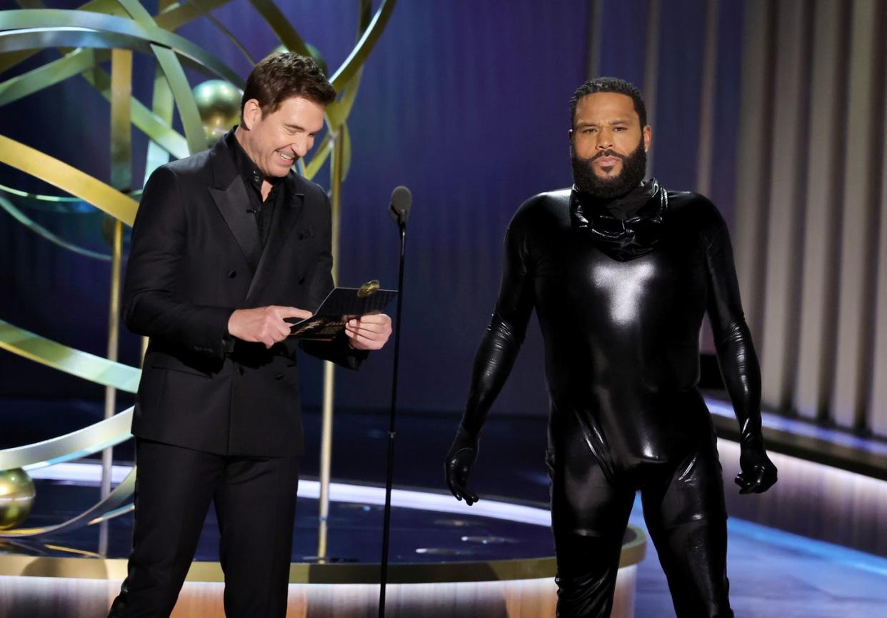 dylan mcdermott and anthony anderson at the 2023 emmys, mcdermott laughs as he holds the envelope with the name of the winner of best actor in a drama limited series, while anderson is wearing a rubber man costume