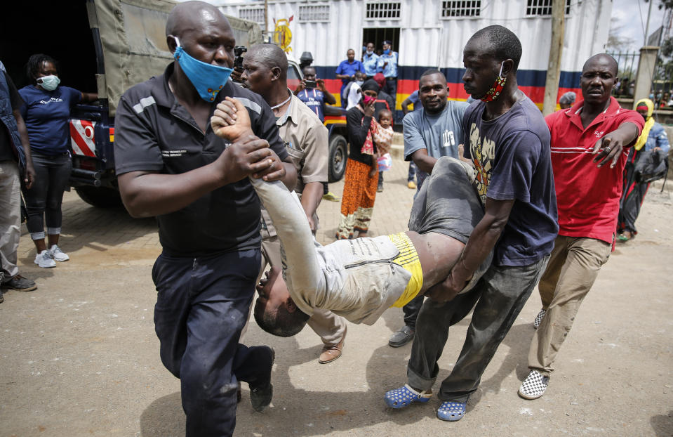 A man who was injured after being trampled is helped away, after residents desperate for a planned distribution of food for those suffering under Kenya's coronavirus-related movement restrictions pushed through a gate and created a stampede, causing police to fire tear gas and leaving several injured, at a district office in the Kibera slum, or informal settlement, of Nairobi, Kenya Friday, April 10, 2020. (AP Photo/Brian Inganga)