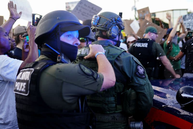 Police officers escort a police SUV from a crowd of protesters while bottles of water are thrown at them during a rally against racial inequality and the police shooting death of Rayshard Brooks, in Atlanta