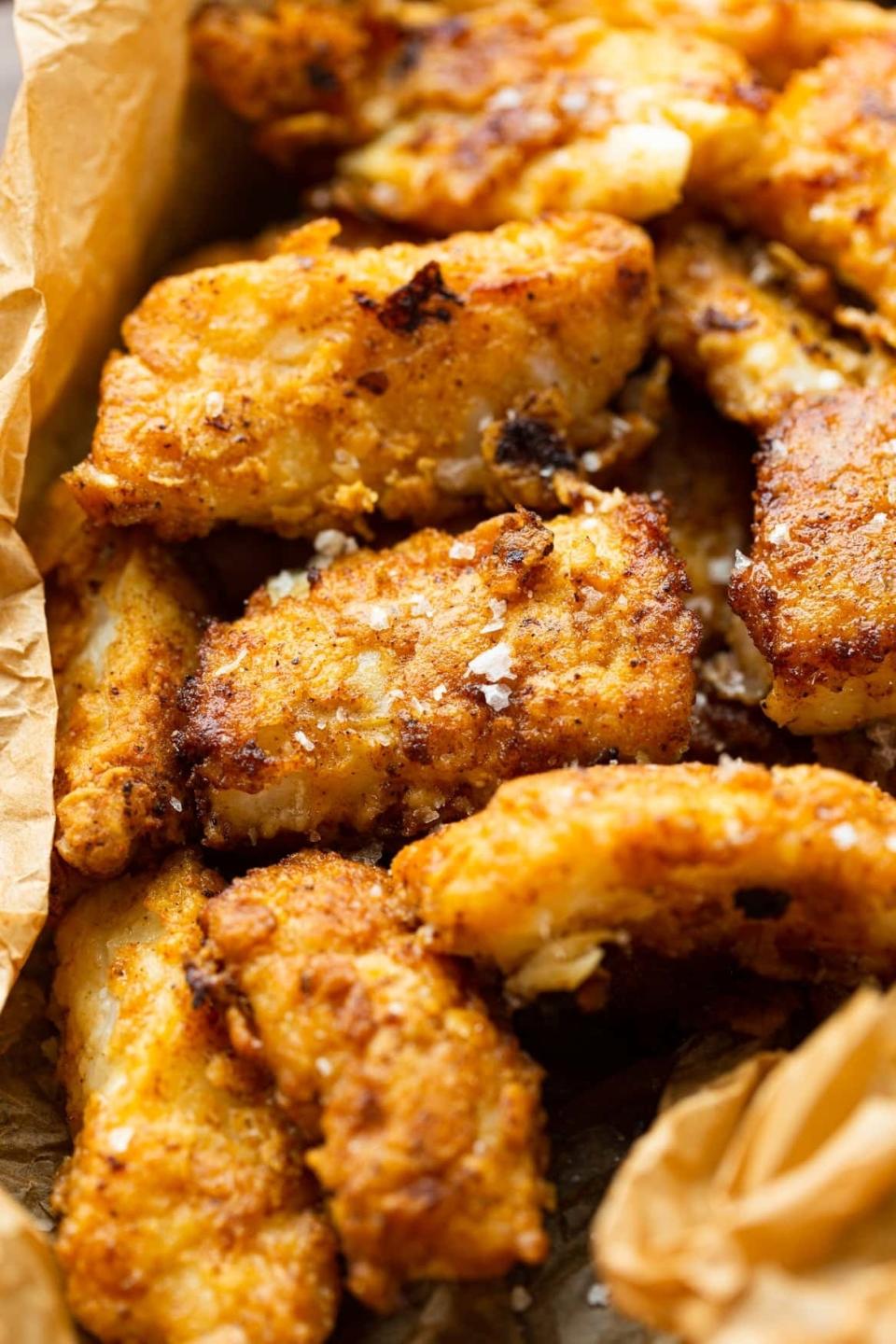 Close-up of several pieces of golden, crispy fried fish on parchment paper. The fish looks well-seasoned and freshly cooked