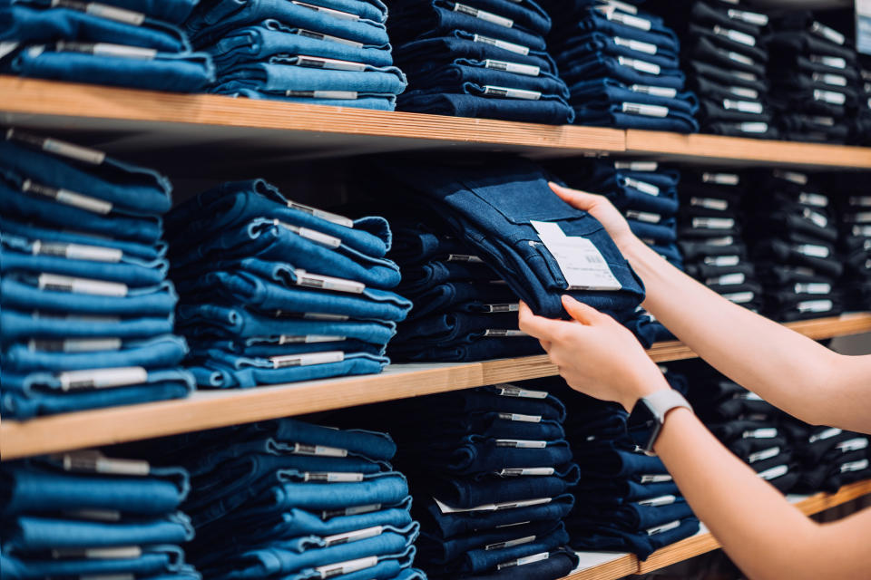 A person holding a pair of blue jeans off a shelf.