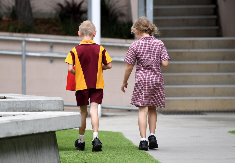 A little boy and little girl wearing school uniforms are seen entering a primary school in Brisbane, Queensland.