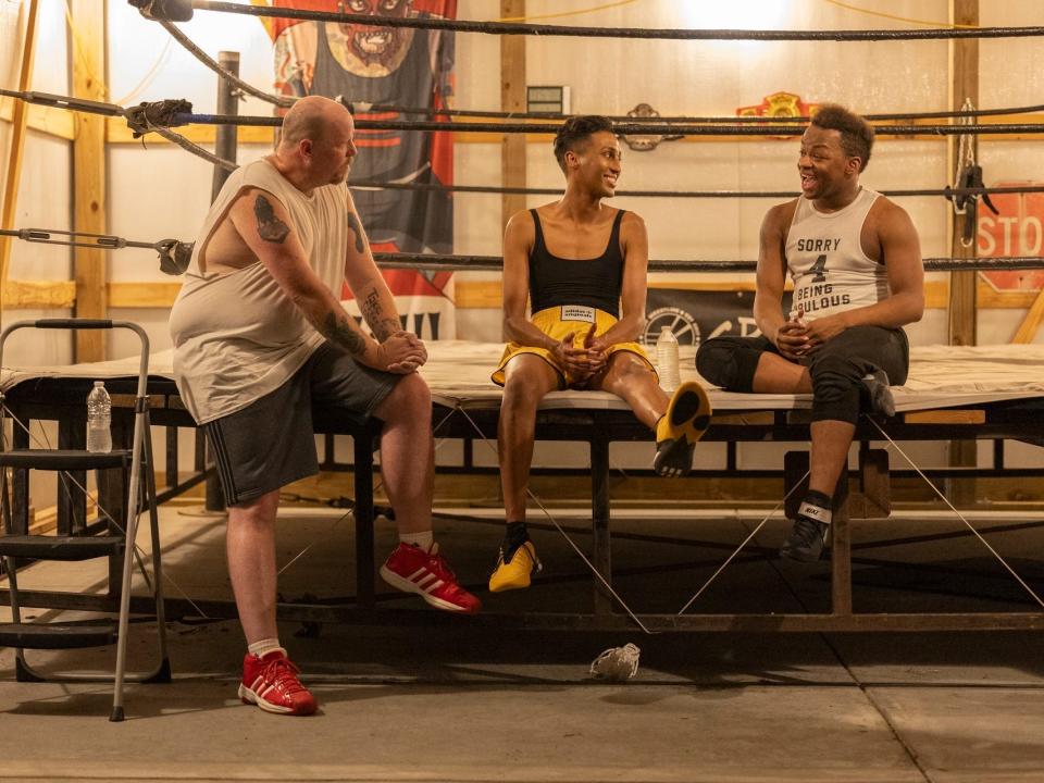 brian, priayanka, and princey on season four of we're here. they're all dressed in athletic wear, sitting casually on the edge of a wrestling while chatting and smiling