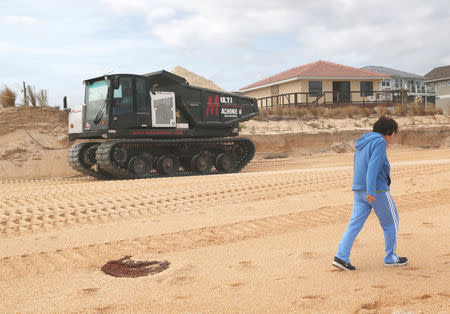 A local resident walks past a tracked vehicle being used to haul sand to replenish the heavily eroded shoreline at Flagler Beach, Florida, U.S., January 26, 2018. Picture taken January 26, 2018. REUTERS/Gregg Newton