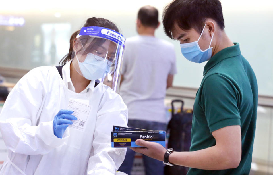 圖為在桃園機場入境管制區內，防疫人員將快篩試劑交給剛下機的旅客。（范揚光攝）