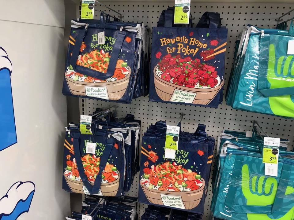 Reusable grocery bags for sale at Sack N Save feature illustrations of poke below phrases including "Hawaii's Home for Poke" and "Hurray for Poke"