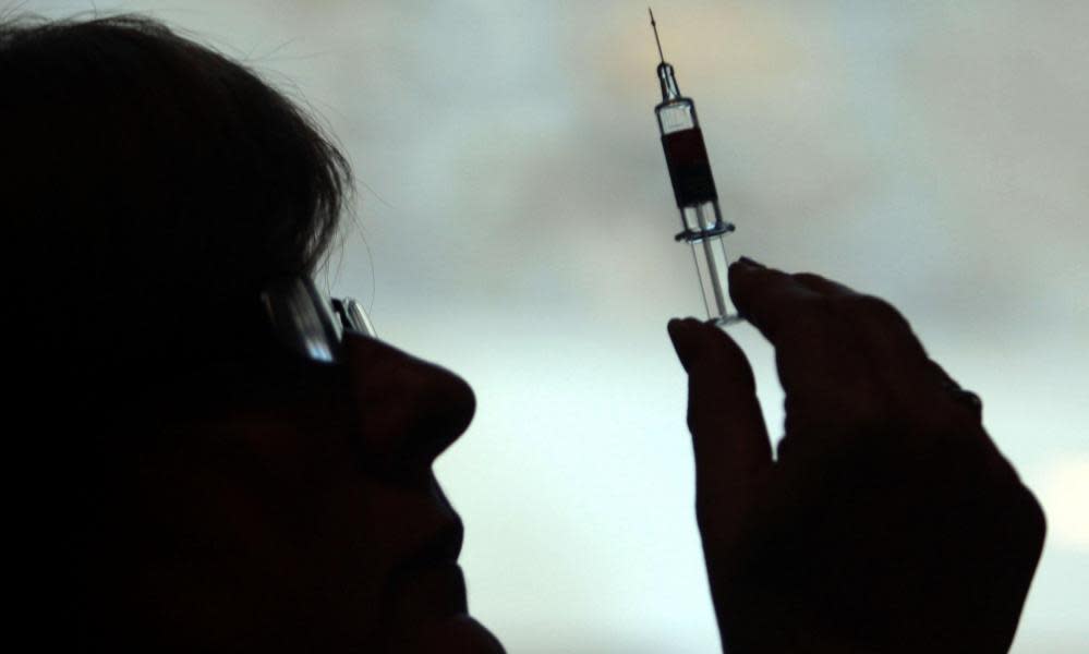 Silhouetted doctor holds up a syringe.