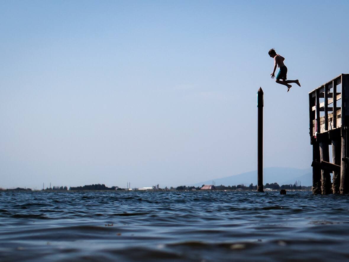 Forecasters say British Columbia should prepare for hotter than normal temperatures in June. A young boy is silhouetted as he jumps off the pier at Crescent Beach into Boundary Bay, in Surrey, B.C., Tuesday, July 6, 2021. (Darryl Dyck/The Canadian Press - image credit)