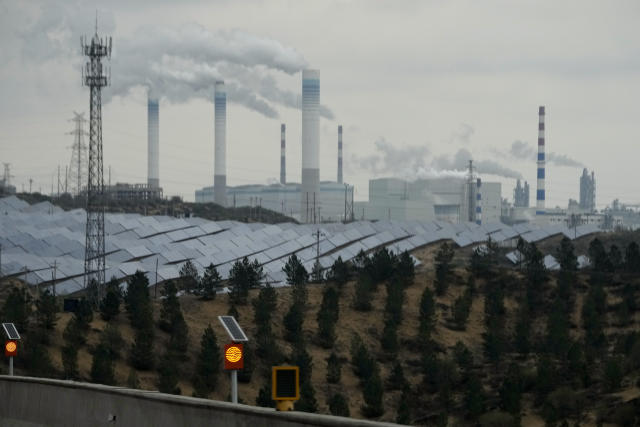 Smoking chimneys and solar panel farm are seen along a highway in a coal producing region in Yulin in northwestern China's Shaanxi province, April 24, 2023. Energy security concerns, worsened by the war in Ukraine, and policy support from rich countries are likely to help investments in clean energy outpace spending on fossil fuels, the International Energy Agency said in a report issued Thursday, May 25, 2023. (AP Photo/Ng Han Guan)